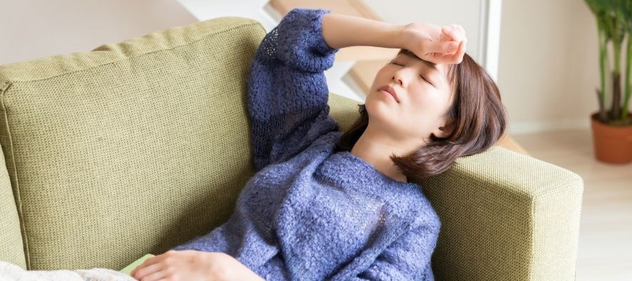 A woman is taking a short nap, with her head resting on the arm of a sofa and one hand resting on her forehead.