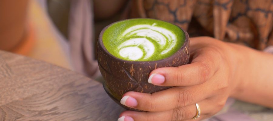 A close-up image of a woman holding a matcha latte in her hand.