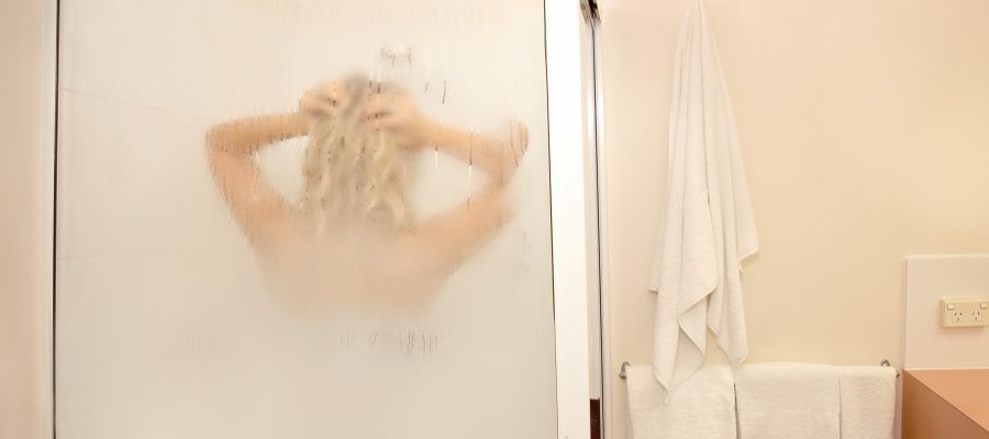 Image of a short blond haired woman taking a steamy shower, which can help with melatonin production to help you fall asleep.