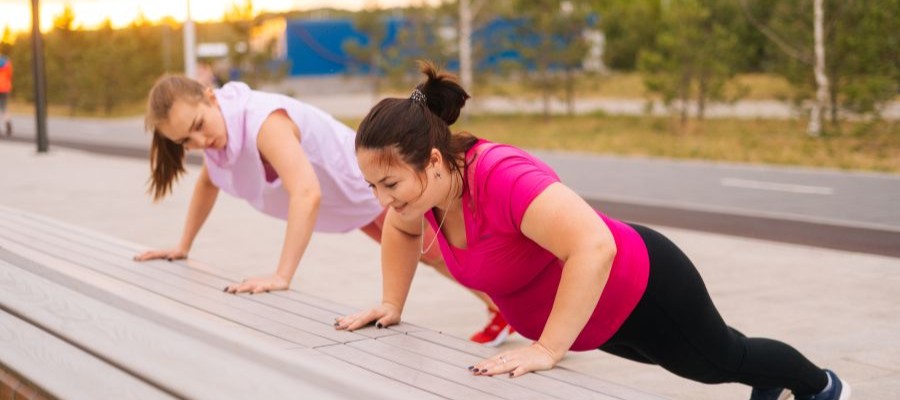 Two women do modified push-ups against a bench during an early morning workout.