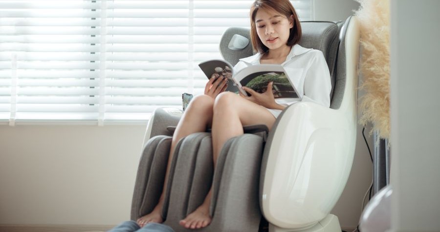 A woman sits in a massage chair, reading a magazine. 