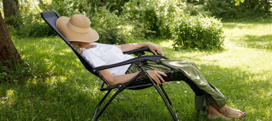 A woman is taking a nap on a lawn chair outside. She has a straw hat covering her face. 