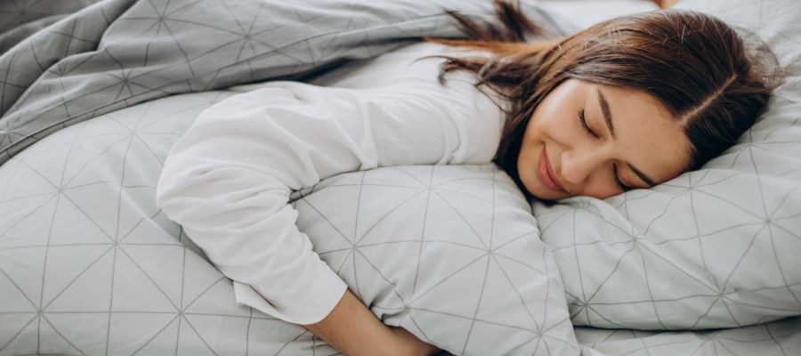 A woman sleep on her stomach a pillow under her head and another one under her arm.