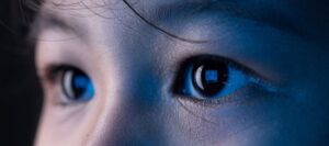 A close up image of a young person's eyes, staring at a screen which you can see in the reflection of their pupils.