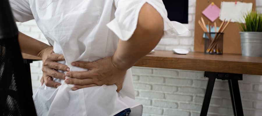 Image of a person holding their hands on their lower back, as though they have back pain from sitting at a desk. 