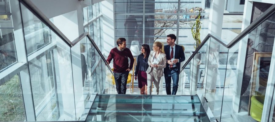 An image of 4 coworkers walking up the stairs in a large office building.