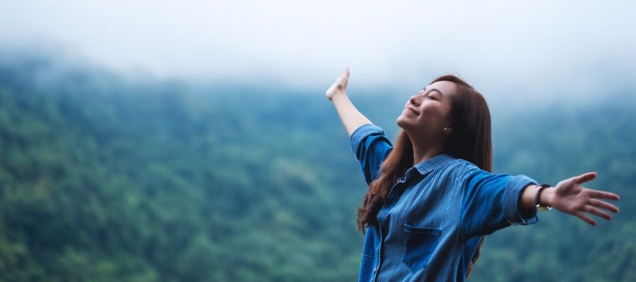 A woman stands with her face turned to the sky and her arms outstretched. 