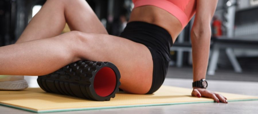 A female uses a foam roller to stretch her hamstring to aid in recovery.