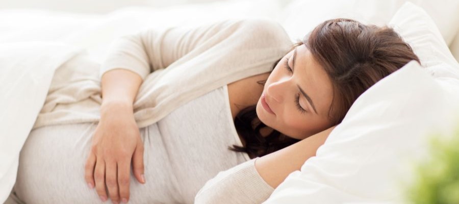 A pregnant woman is lying on her side with one hand resting on her belly. It looks like she is asleep during the middle of the her pregnancy.