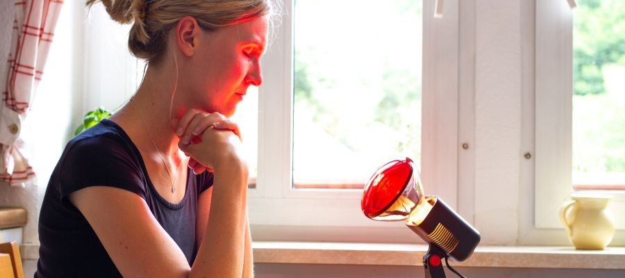 A woman sits with her eyes closed, facing a red light lamp, often used to treat seasonal affective disorder (SAD). 