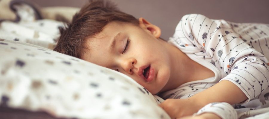 A young child sleep on his side in bed with his mouth slightly open.