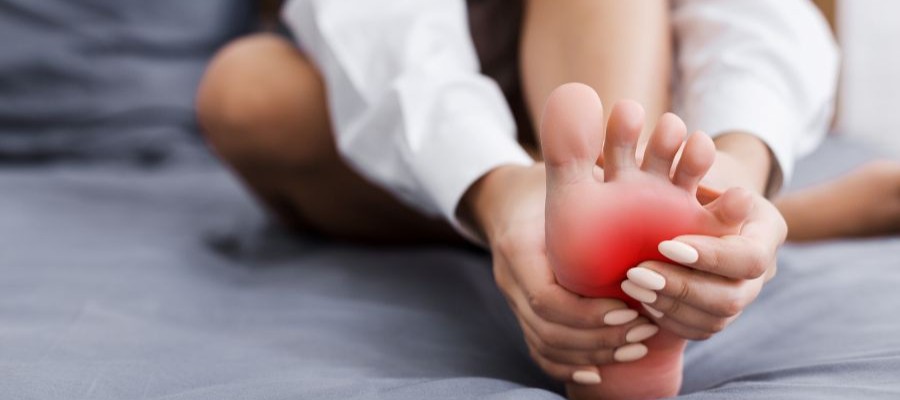 An image of a woman sitting on a bed, holding her foot. It is highlighted in red to indicate pain such as is experienced with restless leg syndrome.