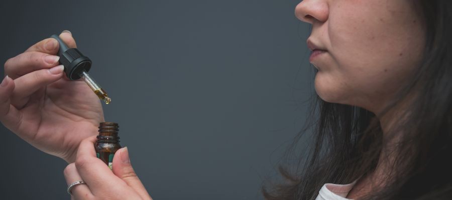 A woman is shown in profile, holding an eye dropper of a tincture. 