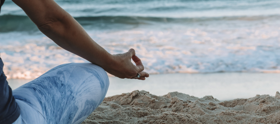 A partial image of a person sitting on the beach, meditating, facing the water.