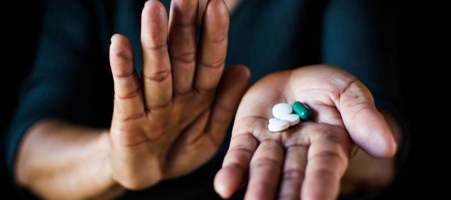 A person holds a variety of pills in one hand and holds up their other hand in a gesture that says stop.